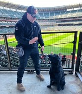photo of man with a black labrador at a stadium