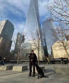 photo of a woman and black lab standing in front of a building